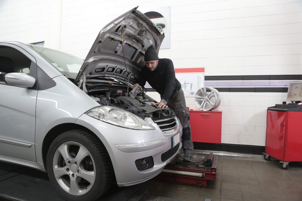 man looking under hood of silver car